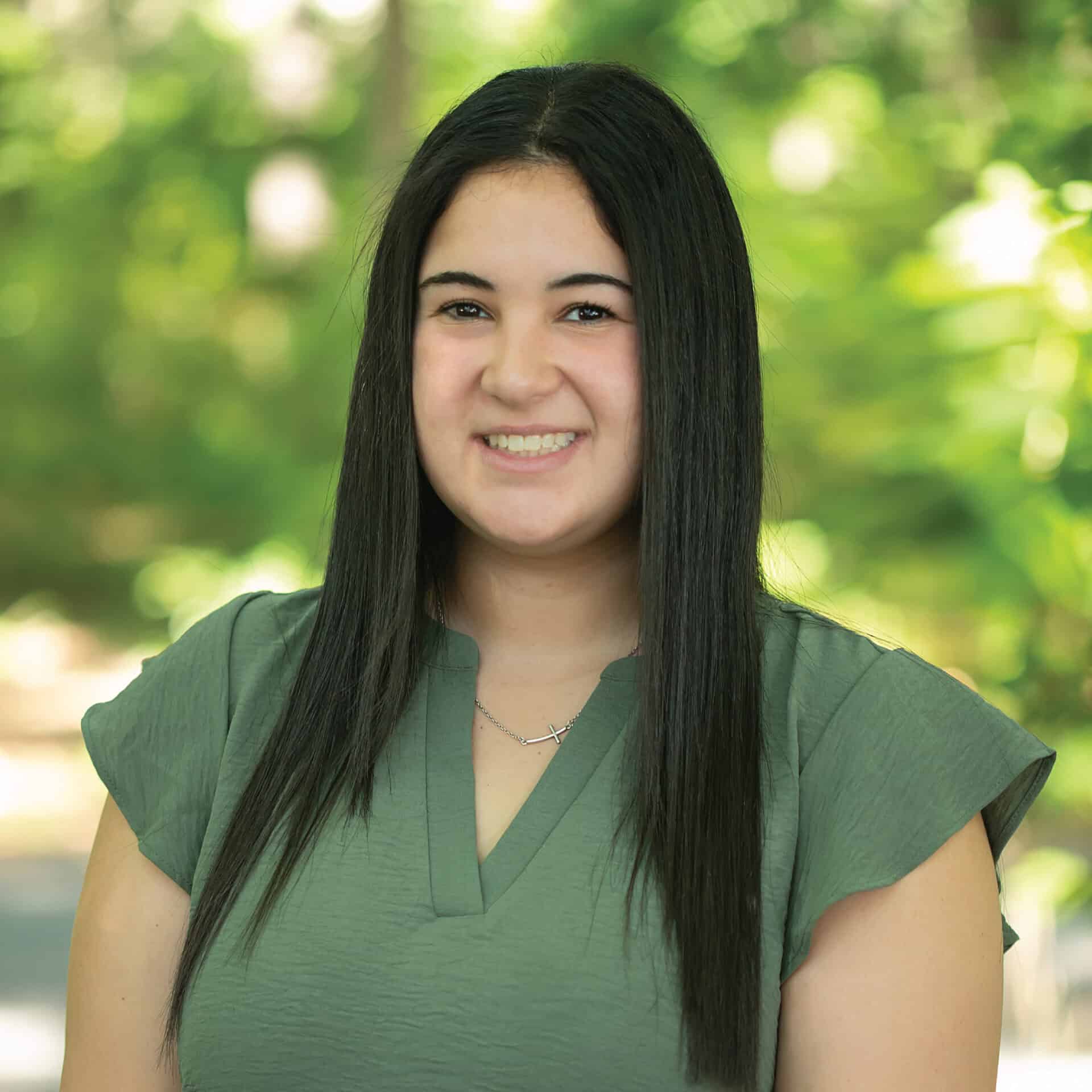 Professional woman smiling outdoors in a park, wearing a green top, representing leadership and confidence for law firm CPA branding.